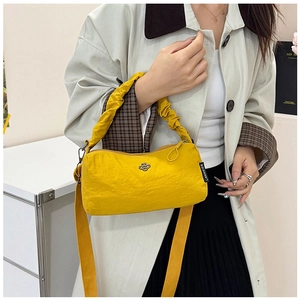 Detail of a bright yellow nylon crossbody bag with floral metal charm and wide shoulder strap
