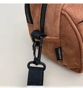 Close-up of brown suede crossbody bag featuring black metal hook and branded side tag