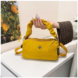Detail of a bright yellow nylon handbag featuring a ruffled handle and metal flower logo