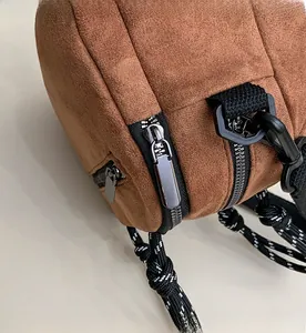 Detailed close-up of dark brown suede bag with black zipper and woven shoulder strap