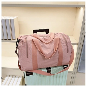 Pink nylon travel bag with Travel embroidery shown on a mint green suitcase handle