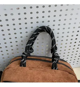 Detail of brown suede handbag featuring creative black and white woven rope handles