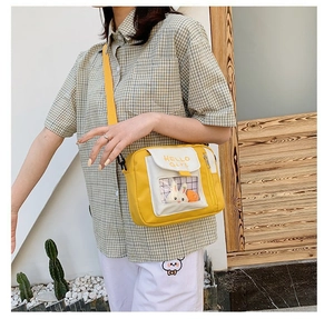 Détail de sac bandoulière en toile jaune avec poche transparente et peluches