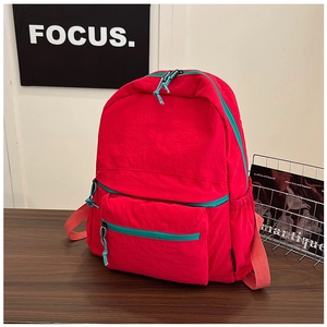 Detail view of red nylon backpack with light red straps and blue zippers on wood surface