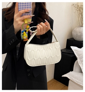 Detailed view of white shoulder bag with wave quilted pattern held by model