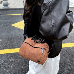 Detail of tan suede crossbody bag featuring woven top handles and front zipper pocket