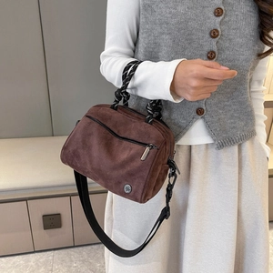 Detailed view of the brown suede crossbody bag featuring a front zipper and rope handle