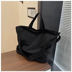 Detail of a large black canvas tote bag with wide shoulder straps on a wooden surface