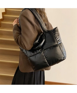 Large black quilted puffer tote bag with glossy finish shown on model in stairwell