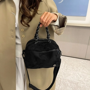 Close-up of black crossbody bag featuring woven rope handle and matte suede texture