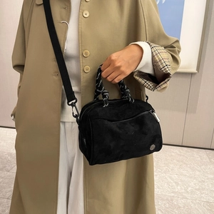 Detail of black crossbody bag with woven handle and wide strap on tan coat