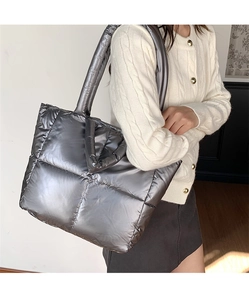 Detail of a large silver quilted tote bag shown on a model in a minimalist home setting