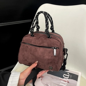 Detail of dark brown suede crossbody bag with braided rope handle and metal logo