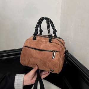 Detail view of brown suede handbag with woven rope handle and metal zipper pocket