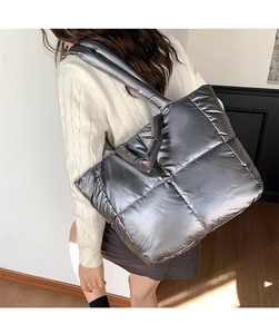 Detailed side view of a large silver quilted puffer tote bag worn by a model in a room