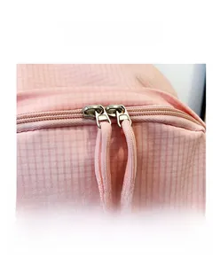 Detailed close-up of pink plaid backpack with durable dual zippers and woven pulls
