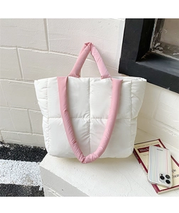 Detailed shot of a white quilted tote bag with pink handles against a white brick wall