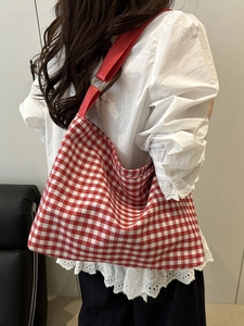 Detail of red checkered canvas tote bag with durable shoulder strap on model