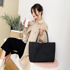 Detail of a large black canvas tote bag styled with a casual trench coat in a city setting
