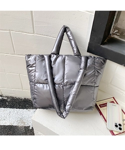 Close-up of a silver quilted tote bag with metallic texture on a white brick background