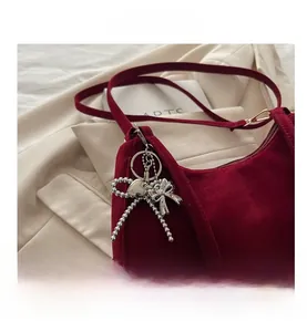 Gros plan du sac baguette bordeaux mat avec breloque nœud argenté et pendentif cœur