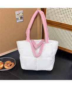 Close-up of white quilted tote bag with pink padded handles on a dark floor