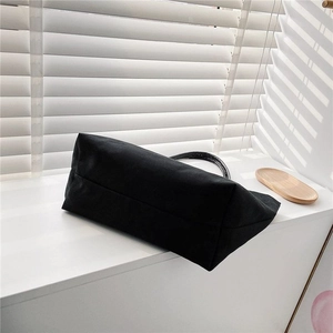 Minimalist black canvas bucket bag shown on a window sill with natural striped shadows