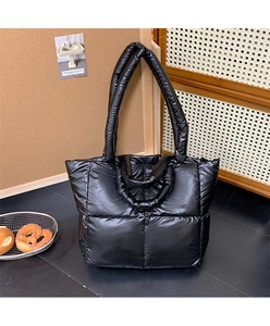 Detail of black quilted puffer tote bag with glossy finish and dual handle design