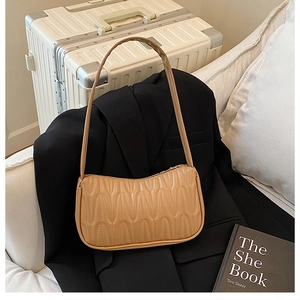Detail view of beige quilted baguette bag with pleated texture on black blazer fabric