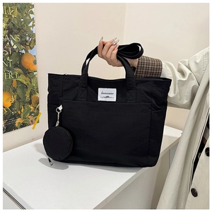 Detail view of black nylon tote bag with white woven label and hanging coin purse accessory