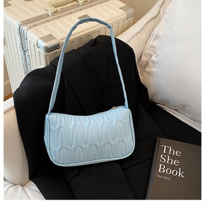 Detail of light blue quilted underarm bag showing wavy texture and gold zipper closure
