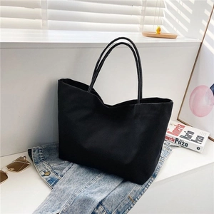 Detail view of a black canvas tote bag on a modern white stand with styling props