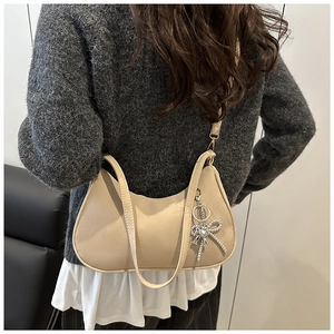 Détail d'un sac demi-lune beige mat avec breloque cœur argentée et fine bandoulière