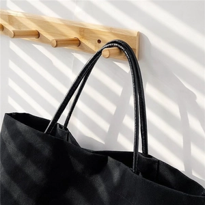 Detail of black canvas bucket bag hanging on a wooden hook with artistic shadow