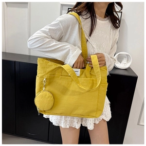 Detail of yellow canvas tote bag featuring a square brand label and a matching coin purse