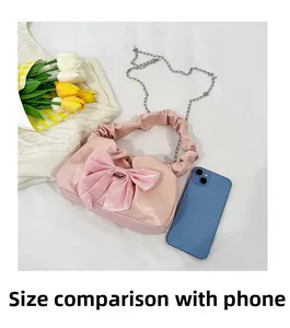 Rosa plissierte Handtasche mit großer Schleife und Kettenriemen neben einem Smartphone