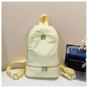 Vue détaillée du sac à dos en nylon jaune pâle avec compartiments zippés sur une table blanche