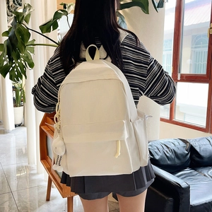 Close-up of cream white canvas backpack with front zipper pocket and plush pendant