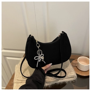 Détail du sac hobo en daim noir avec pendentif nœud argenté sur fond en tricot