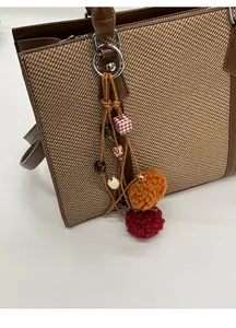 Detail eines gewebten Taschenanhängers mit Holzperlen und Plüschbommeln an Tasche