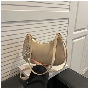 Détail du sac hobo beige mat avec un pendentif en chaîne argentée en forme de nœud