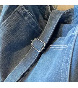 Close-up of washed denim tote bag featuring adjustable metal buckles and white stitching