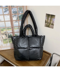 Detail of black quilted puffer tote bag with glossy nylon texture and dual wide straps