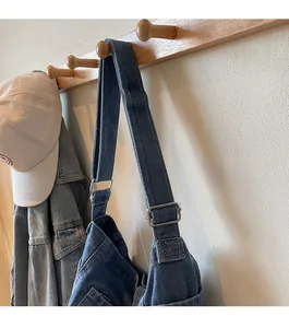 Detail of reinforced stitching and metal hardware on a blue denim crossbody strap