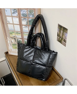 Macro detail of black quilted tote bag with glossy finish and double handle structure
