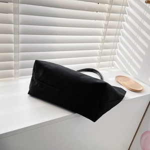 Minimalist black canvas bucket bag shown on a white surface with elegant light and shadows
