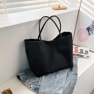 Detail of minimalist black canvas tote bag lying on a denim jacket with natural lighting