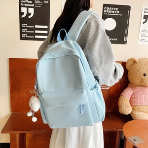 Detail of light blue nylon backpack featuring side drawstring pockets and plush charm