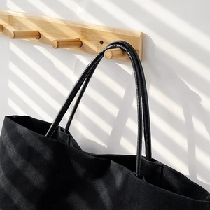 Detail of black canvas bucket bag with leather handles shown in artistic sunlight and shadows