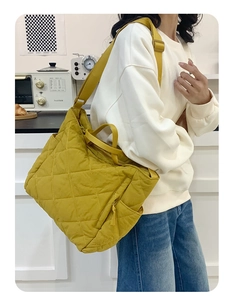 Detail of yellow quilted tote bag featuring adjustable wide strap and side storage pocket